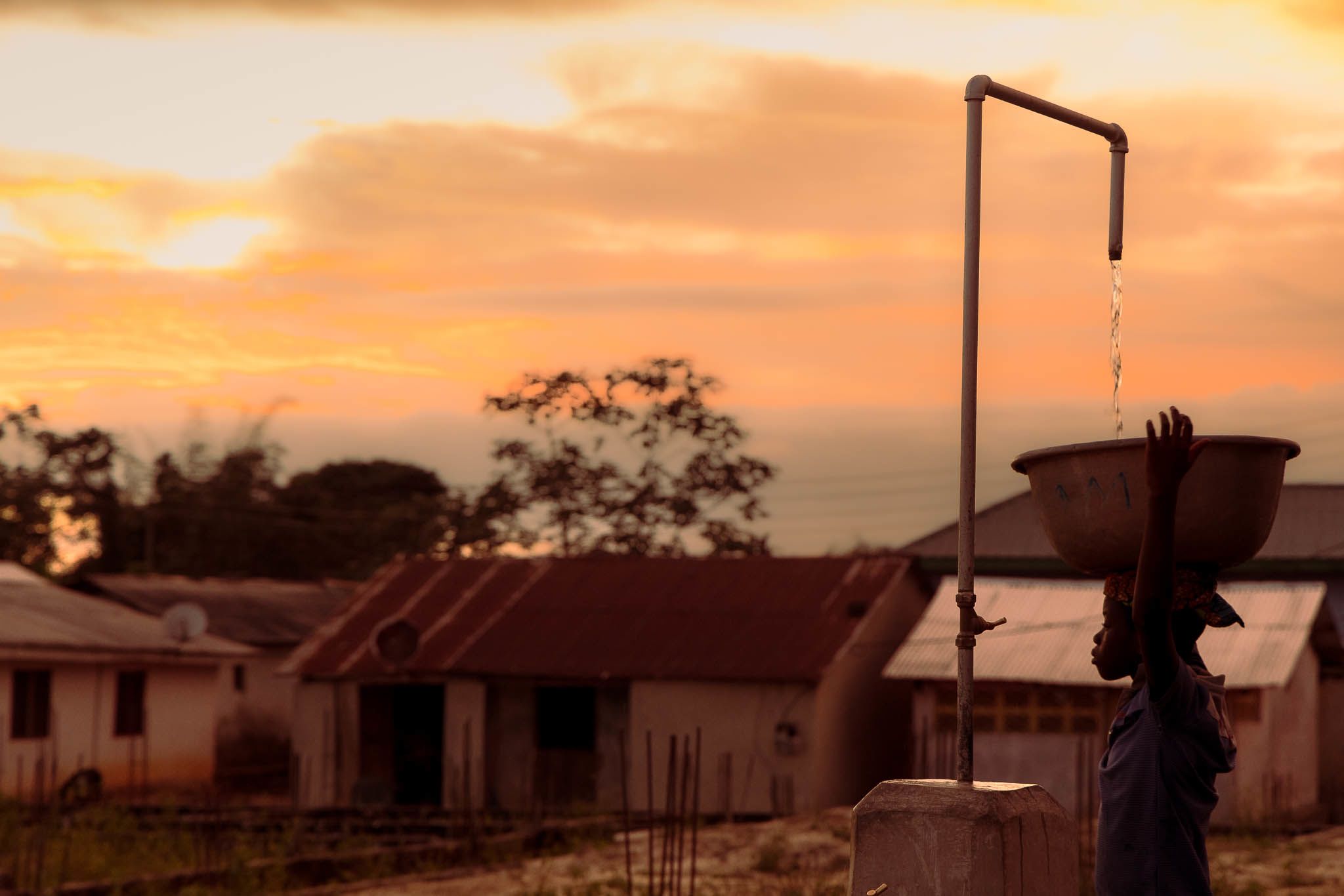 Young Ghanaian boy fetches water from standpipes as the sun sets.